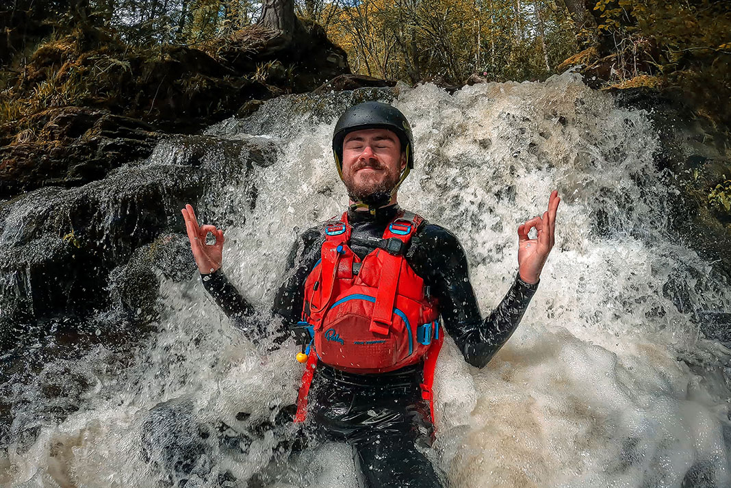 whitewater kayaking man does a yoga pose while sitting in a small forest waterfall