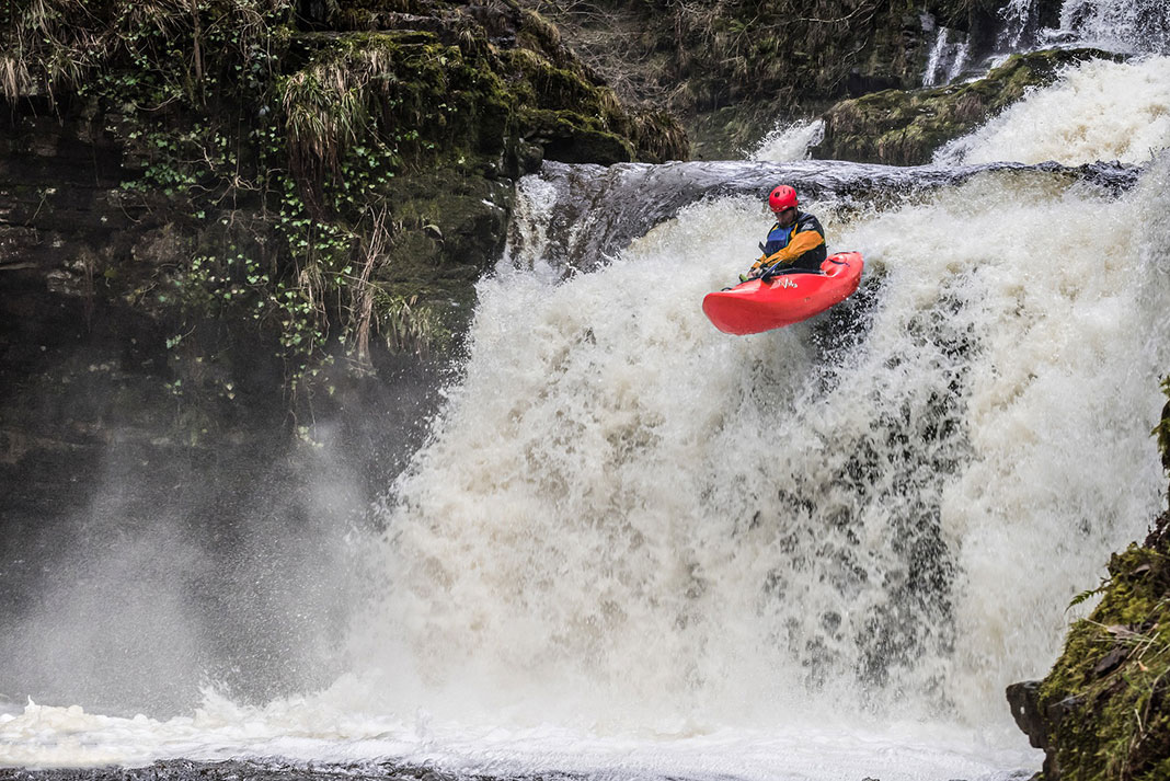man in red whitewater kayak goes over waterfall