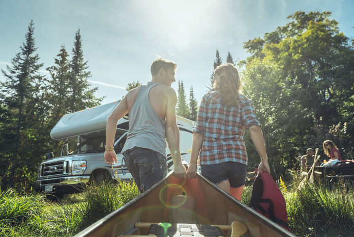 two people pull a canoe toward their camper van in the sunlight