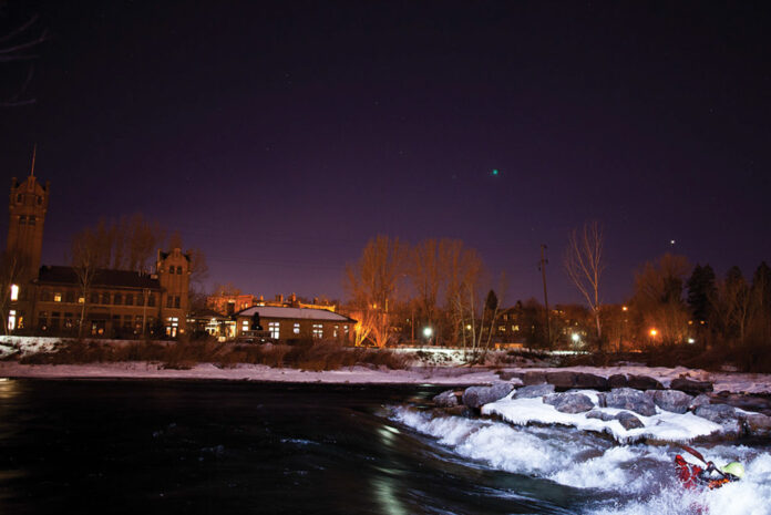 a wintery nighttime scene of a whitewater kayaker paddling Brennan's Wave in Missoula