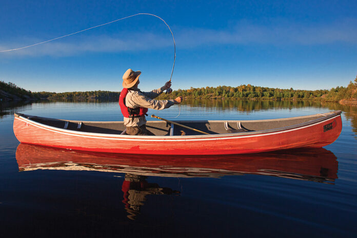 person casts a fly fishing lure from a canoe