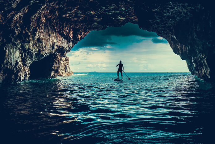 person paddleboarding into a watery cave entrance while wearing an inflatable PFD
