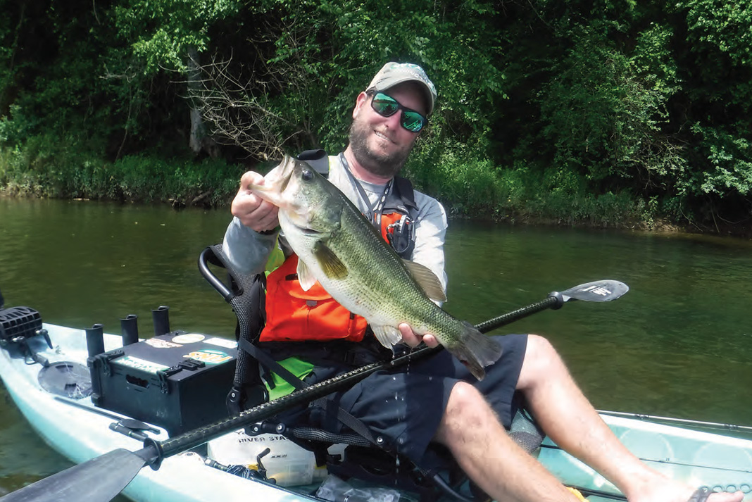 Kayak angler holds up a largemouth bass caught with shad swimbait