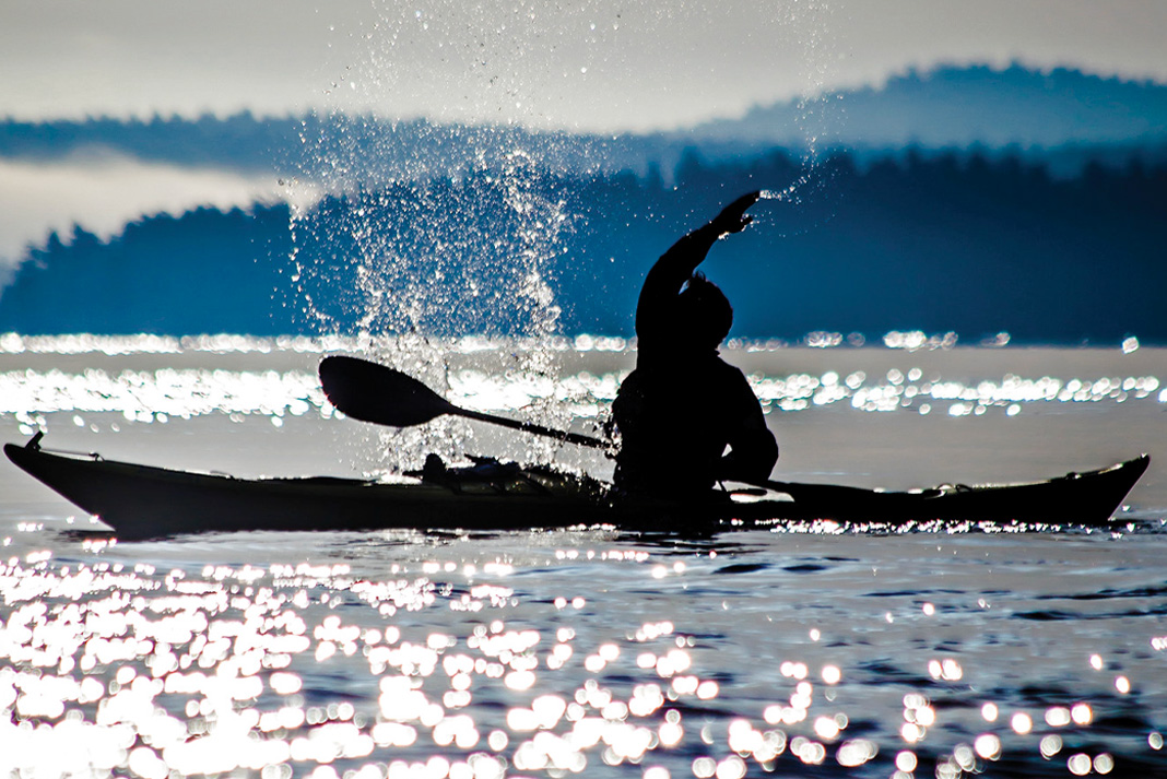 sea kayaker silhouetted while splashing water