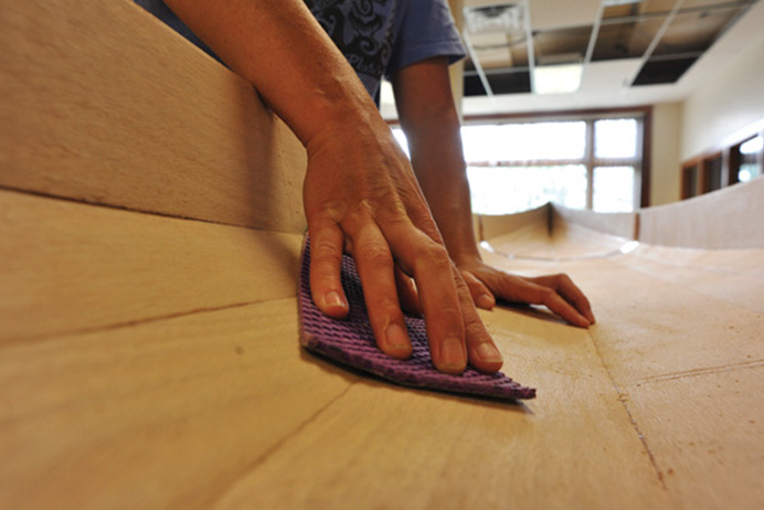 close-up shot of a person's hands sanding the interior of a wooden kayak