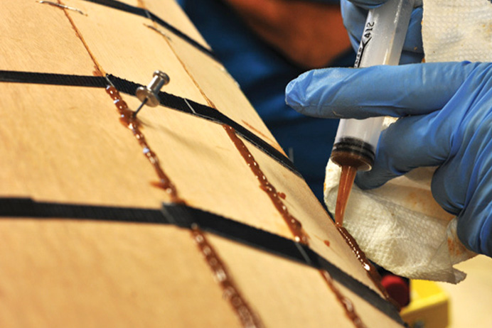 gloved hands shooting seams of a wooden kayak with epoxy