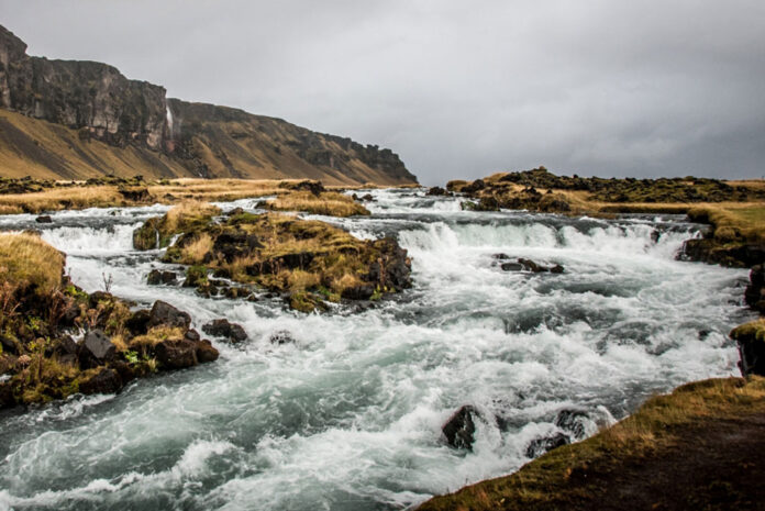 whitewater flows down a river on a cloudy day with hills in the background