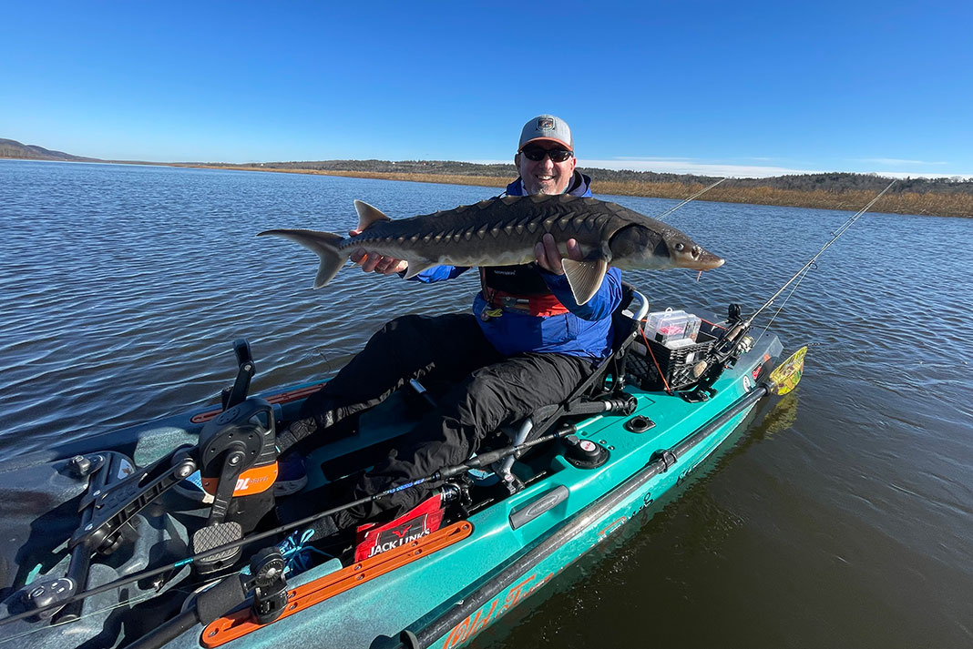 man holds up a large sturgeon caught by fishing from a kayak