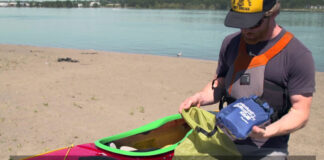 man kneels beside a kayak on the beach packing essential gear