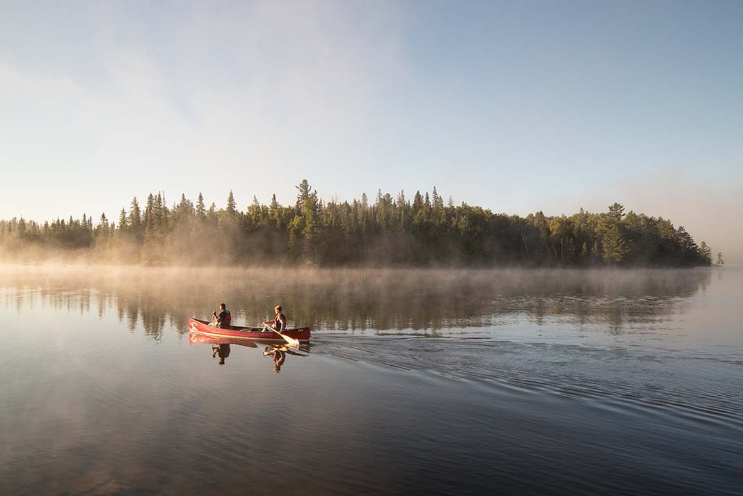 Canoeists paddle across a misty lake in the Algonquin Park backcountry