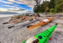 a group of touring kayaks rest on a pebble beach under a vibrant sky