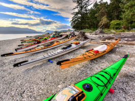 a group of touring kayaks rest on a pebble beach under a vibrant sky