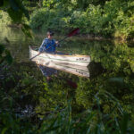Canoe Review: Stellar Kayaks Dragonfly woman paddling the Stellar Kayaks Dragonfly canoe along a leafy, still river