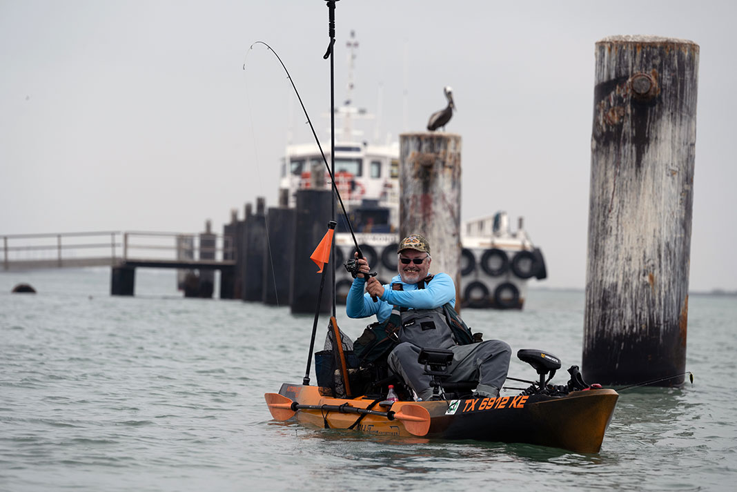 man reels in a fish from an orange fishing kayak on the Texas coast