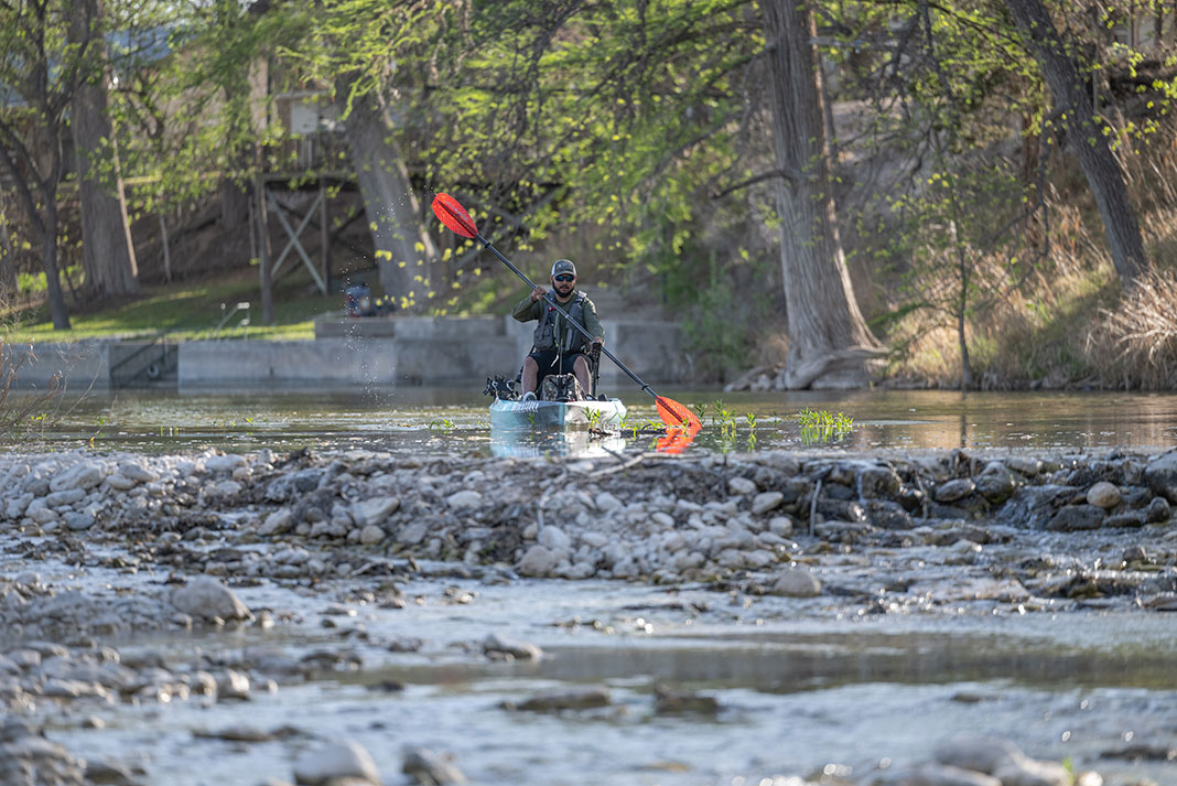man paddles a fishing kayak down the Frio River in Texas hill country