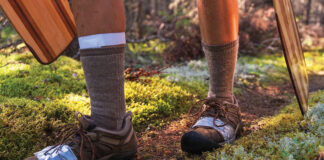 person carrying paddles along a mossy portage trail with shoes wrapped in duct tape