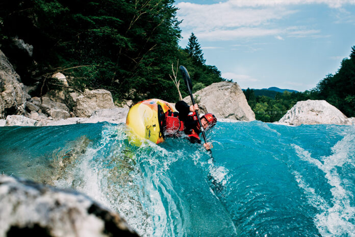 whitewater kayaker tilts sideways above a steep rapid in vibrant blue water