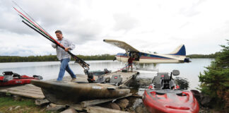man carries fishing gear from a float plane at a remote fishing destination