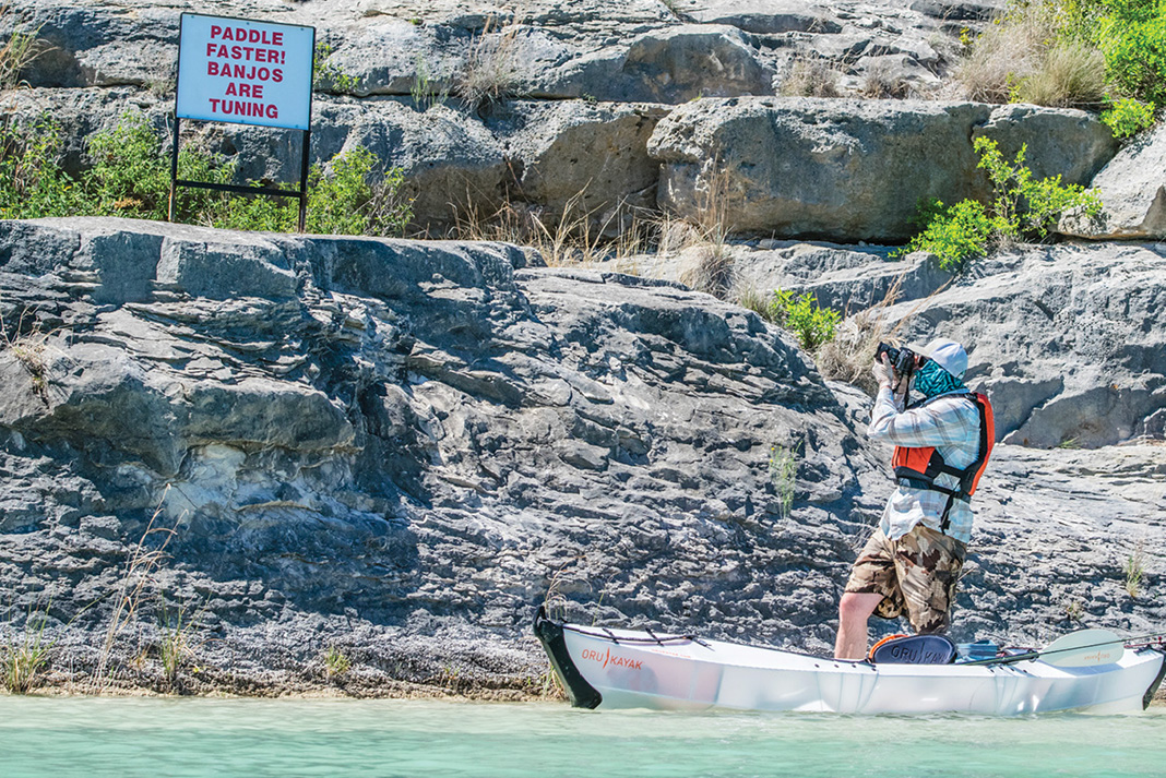photographer stands beside kayak to take photo of a funny sign warning, "Paddle faster! Banjos are tuning"
