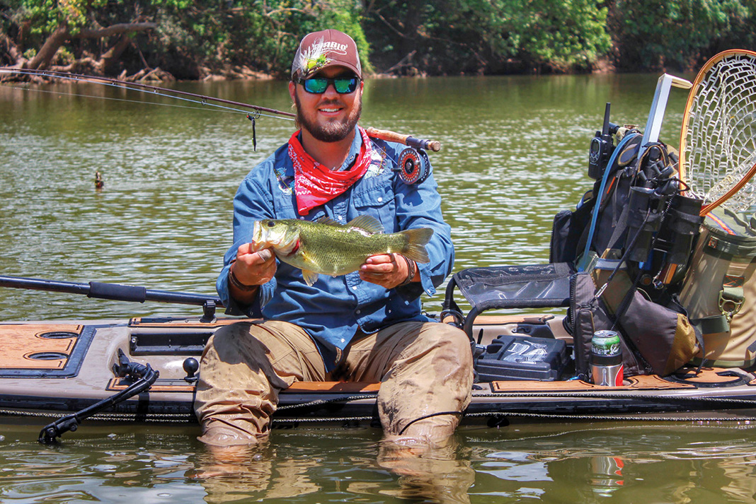 man sits on kayak holding bass he caught and shares sight fishing tips