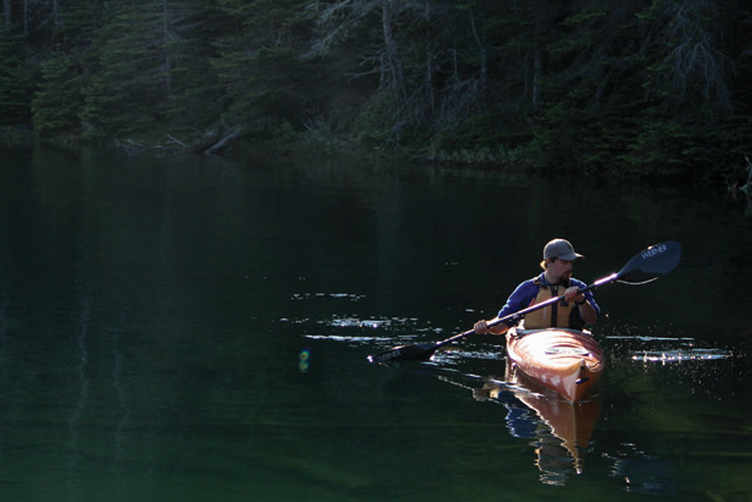 man canoes in sunshine along shadowy Lake Superior shoreline