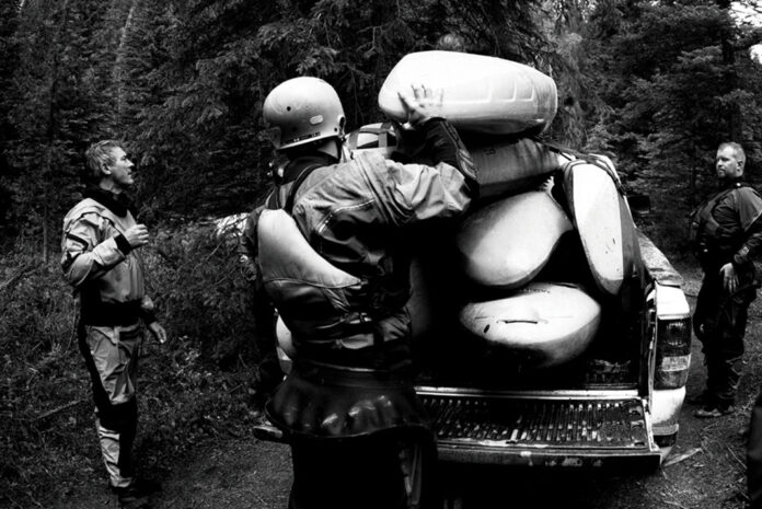 three local river legends stand around in drysuits loading kayaks into a truck bed