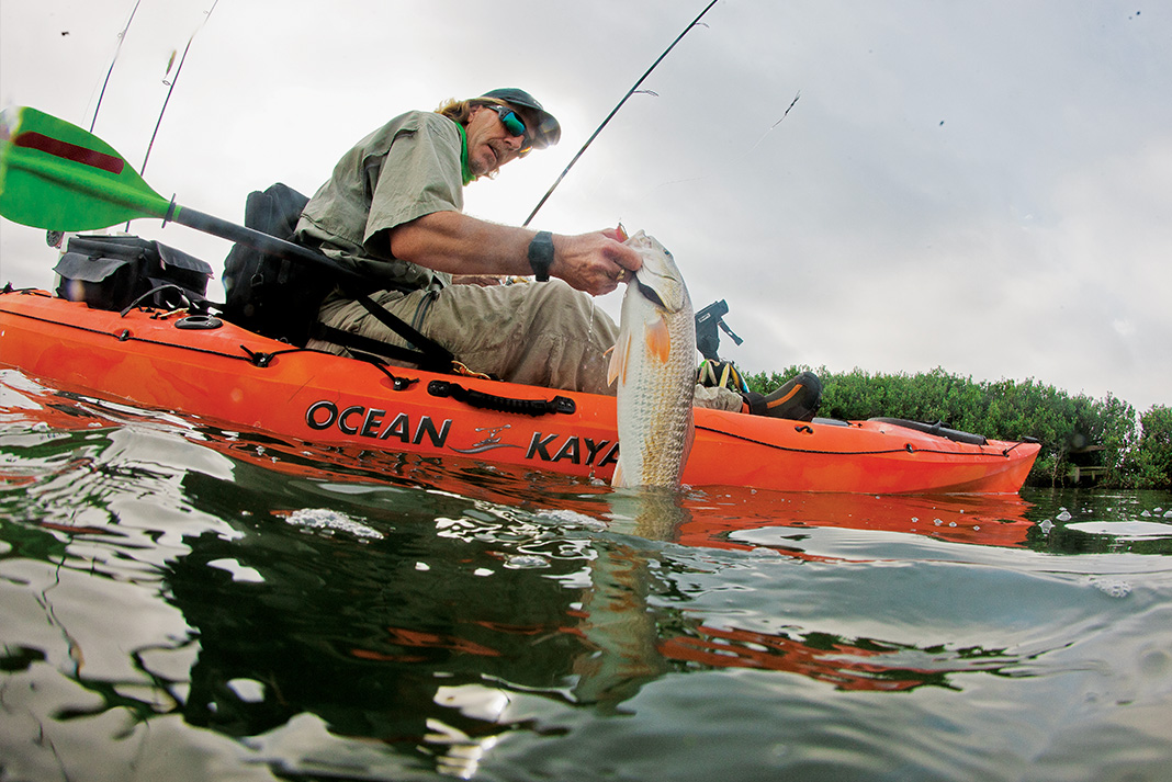 fisheye view of a man living a fish from the water on his Ocean Kayak
