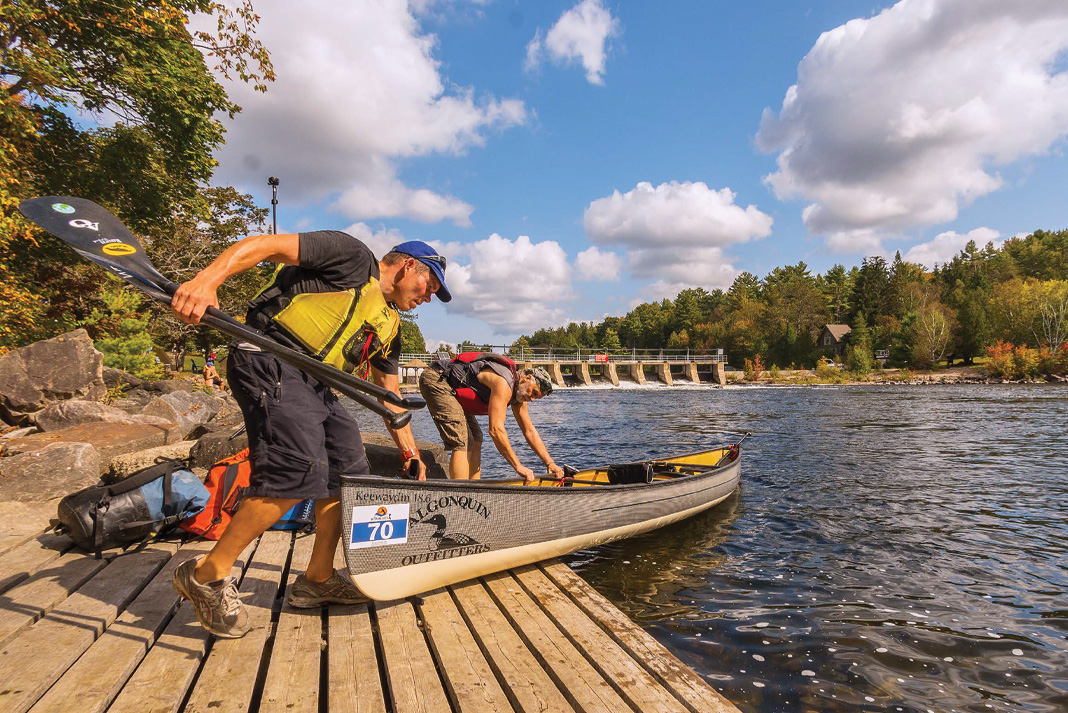 two men portage a canoe near a dam during the Muskoka River X paddling race