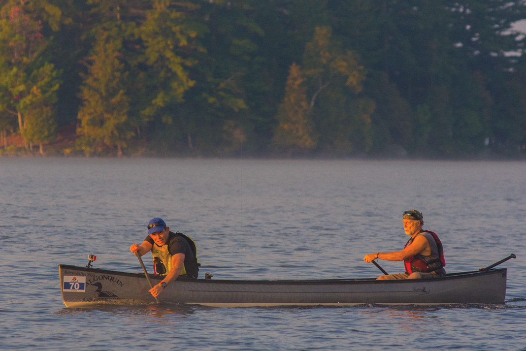 Two men paddle a canoe in golden light at the start of the Muskoka River X race