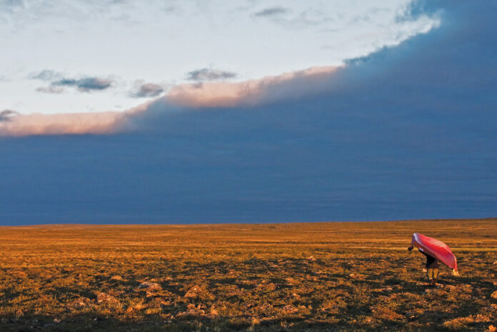 person portages a red canoe across a wide open field