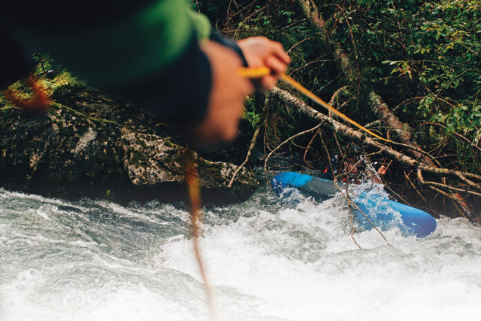 person uses a rope and knife to rescue a whitewater kayaker who is trapped