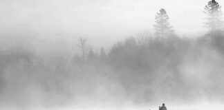 person paddles a canoe through the mist