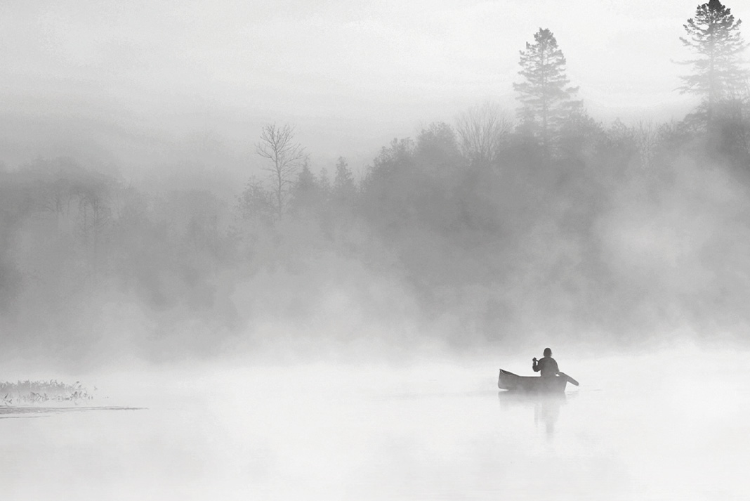 person paddles a canoe through the mist