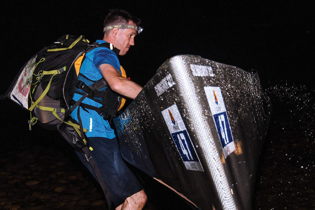 canoeist wearing a headlamp and large backpack lifts a canoe at night time