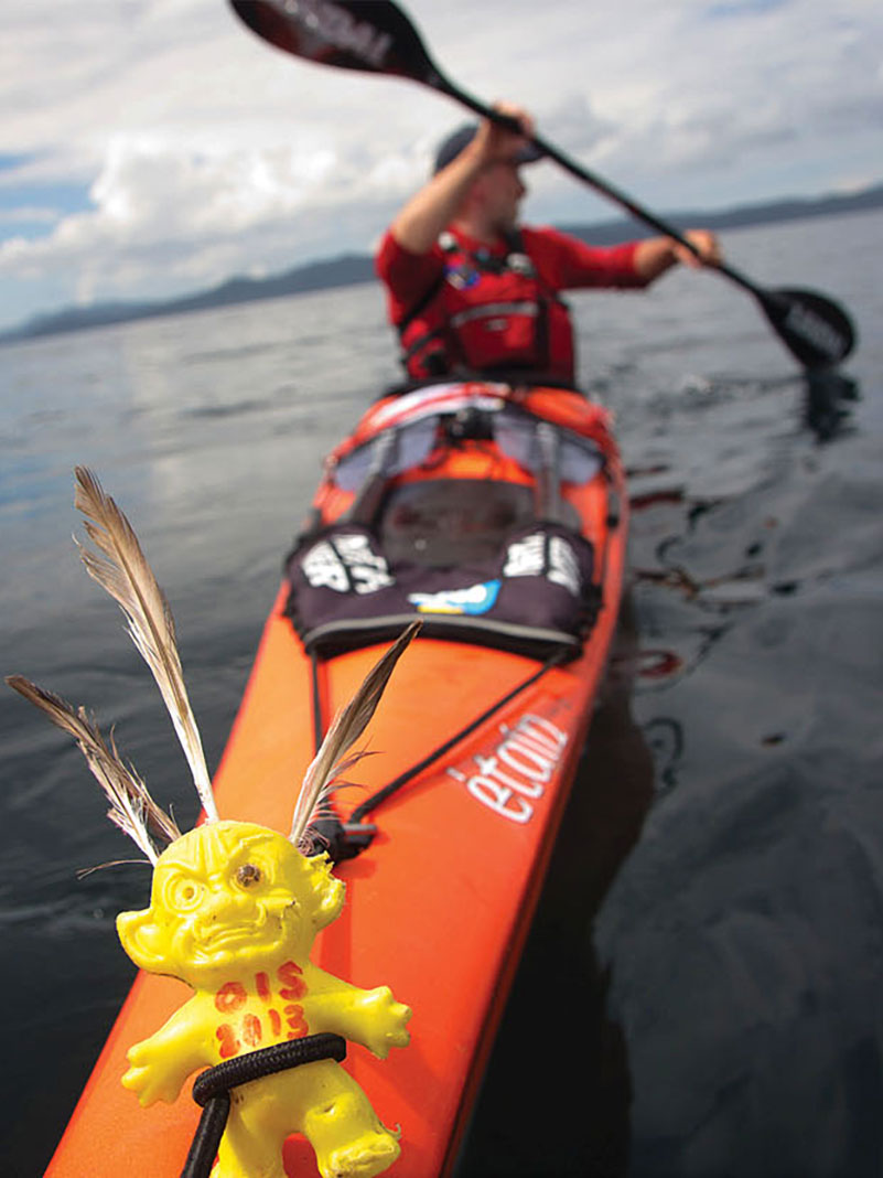 citizen science kayaker paddles with yellow ghoul doll tied to the bow of his boat