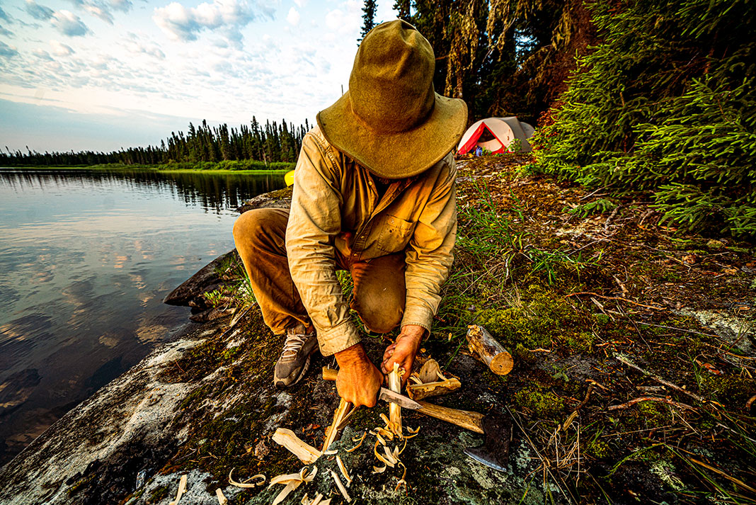 man starts a campfire with wood shavings on the Winisk River