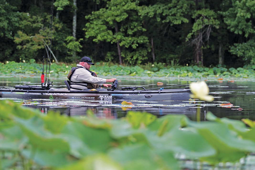 man looks at his fish finder while kayak fishing on a leafy river
