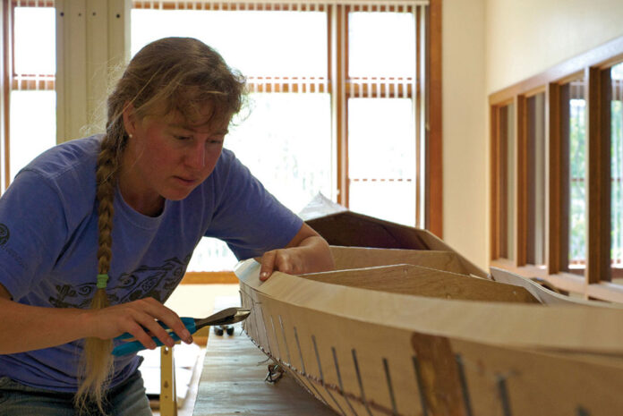 woman works on building a Pygmy Murrelet kayak in a workshop