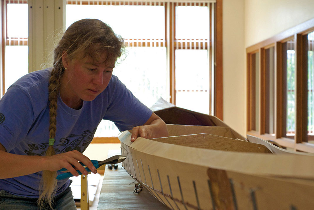 woman works on building a Pygmy Murrelet kayak in a workshop