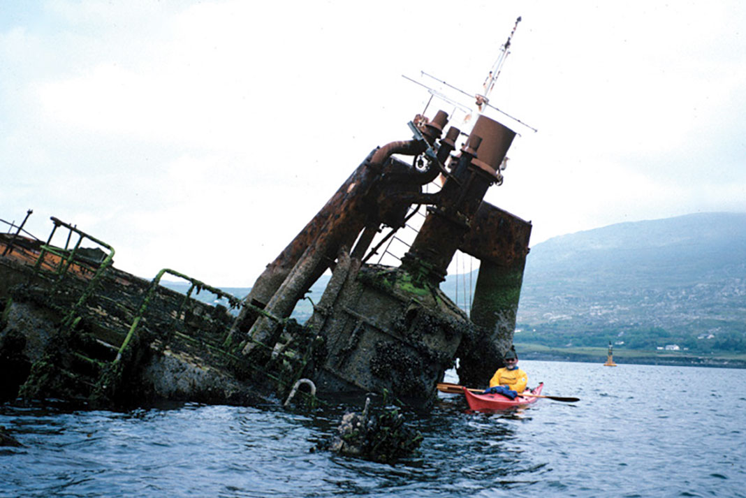 Frank Goodman poses beside an Irish shipwreck in his sea kayak