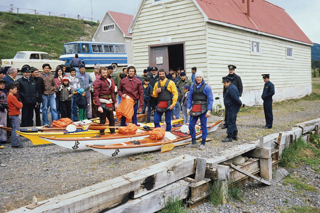 four expedition sea kayakers pose before setting off with a crowd and several police officer standing behind them