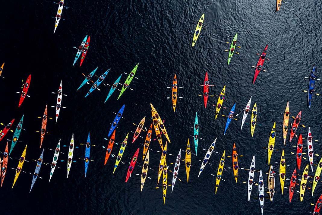 overhead view of a large, multicolored group of sea kayaks on dark water in Comox Lake, BC, Canada