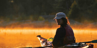 woman in kayak looks back at camera on misty water at dawn