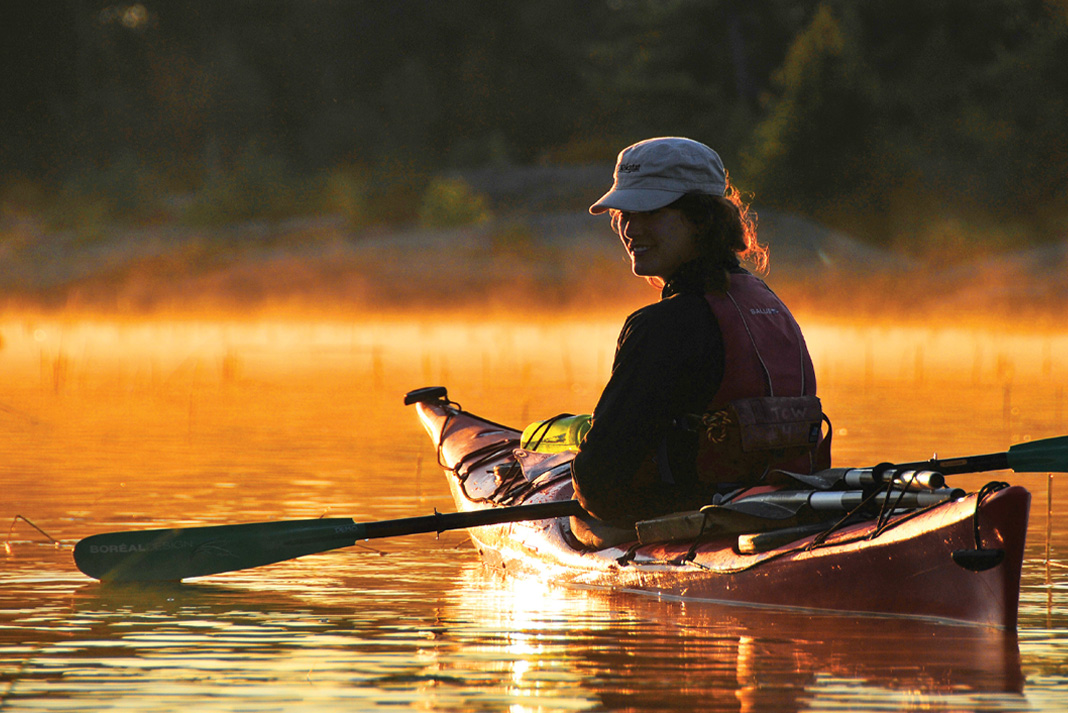 woman in kayak looks back at camera on misty water at dawn