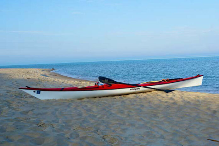 red touring kayak sits on beach after Lake Michigan crossing