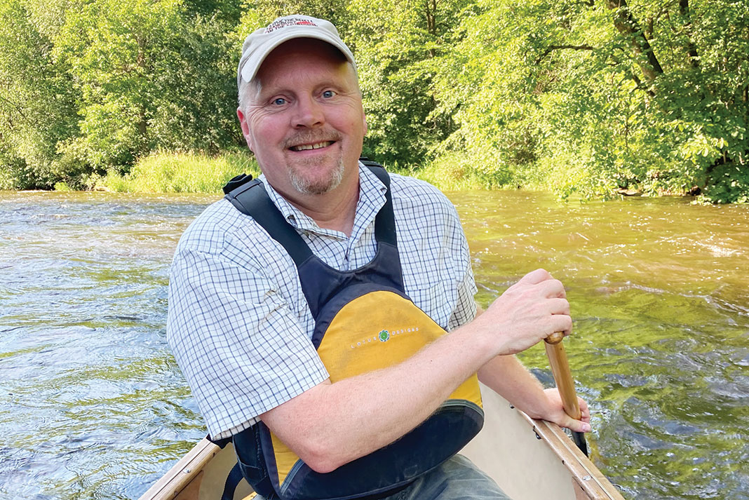 Ed Vater poses in a canoe with paddle in hand on a river after his retirement