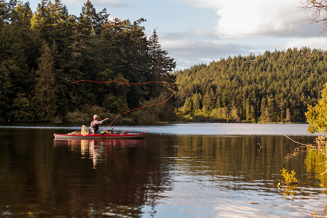 a man fly fishes from a kayak on a serene lake