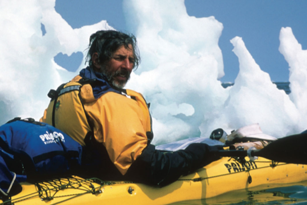 man on arctic kayak expedition poses in front of floating ice in fantastic shapes