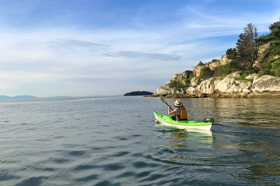 woman in hat paddles past rocky shore on a less ambitious kayak adventure