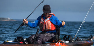 a man lands a fish while wearing an orange kayak fishing life vest